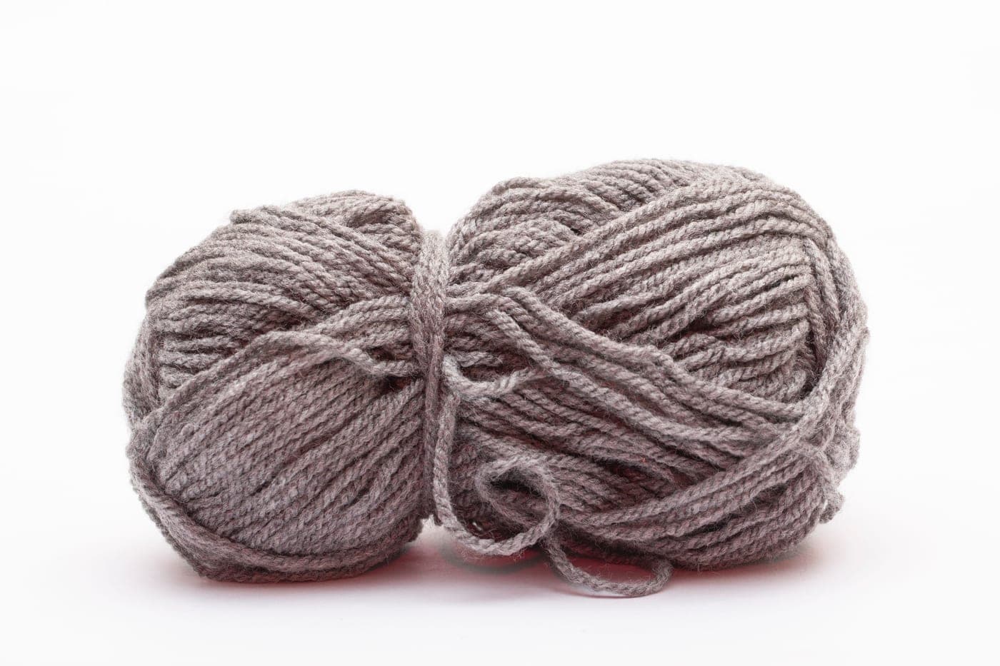 A ball of smooth acrylic yarn beside a skein of woolen-spun wool on a plain surface