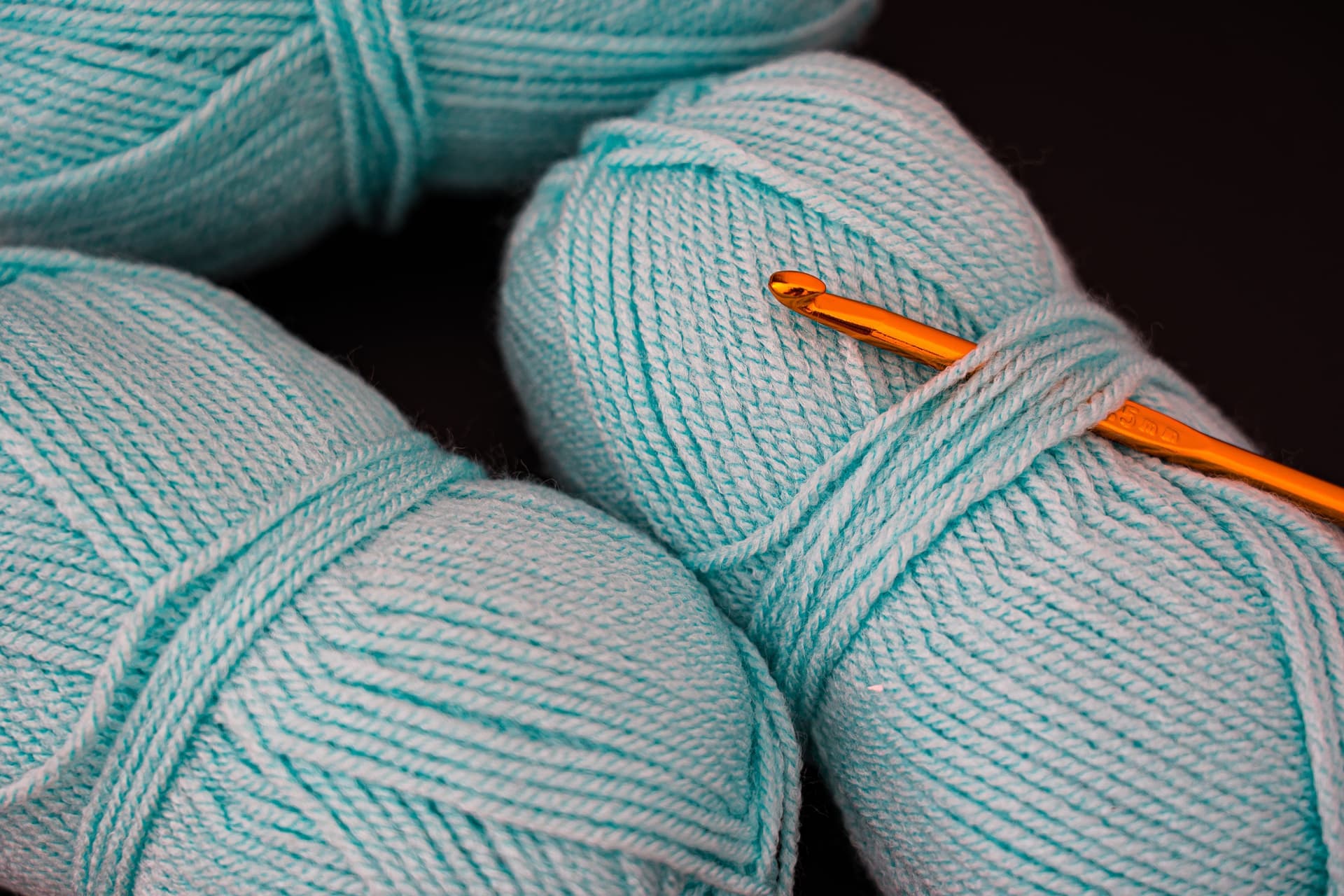 Skeins of wool and cotton yarn beside knitting needles and a crochet hook on a work surface
