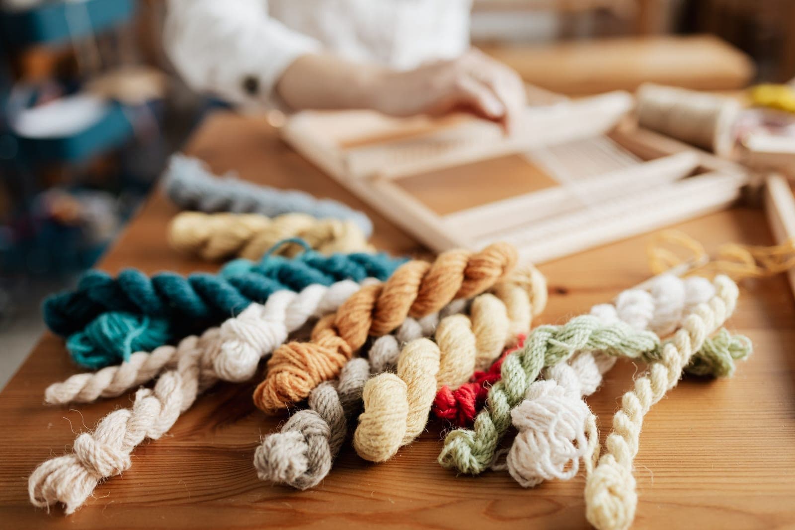 Skeins of wool and cotton yarn in muted colors arranged on a wooden surface